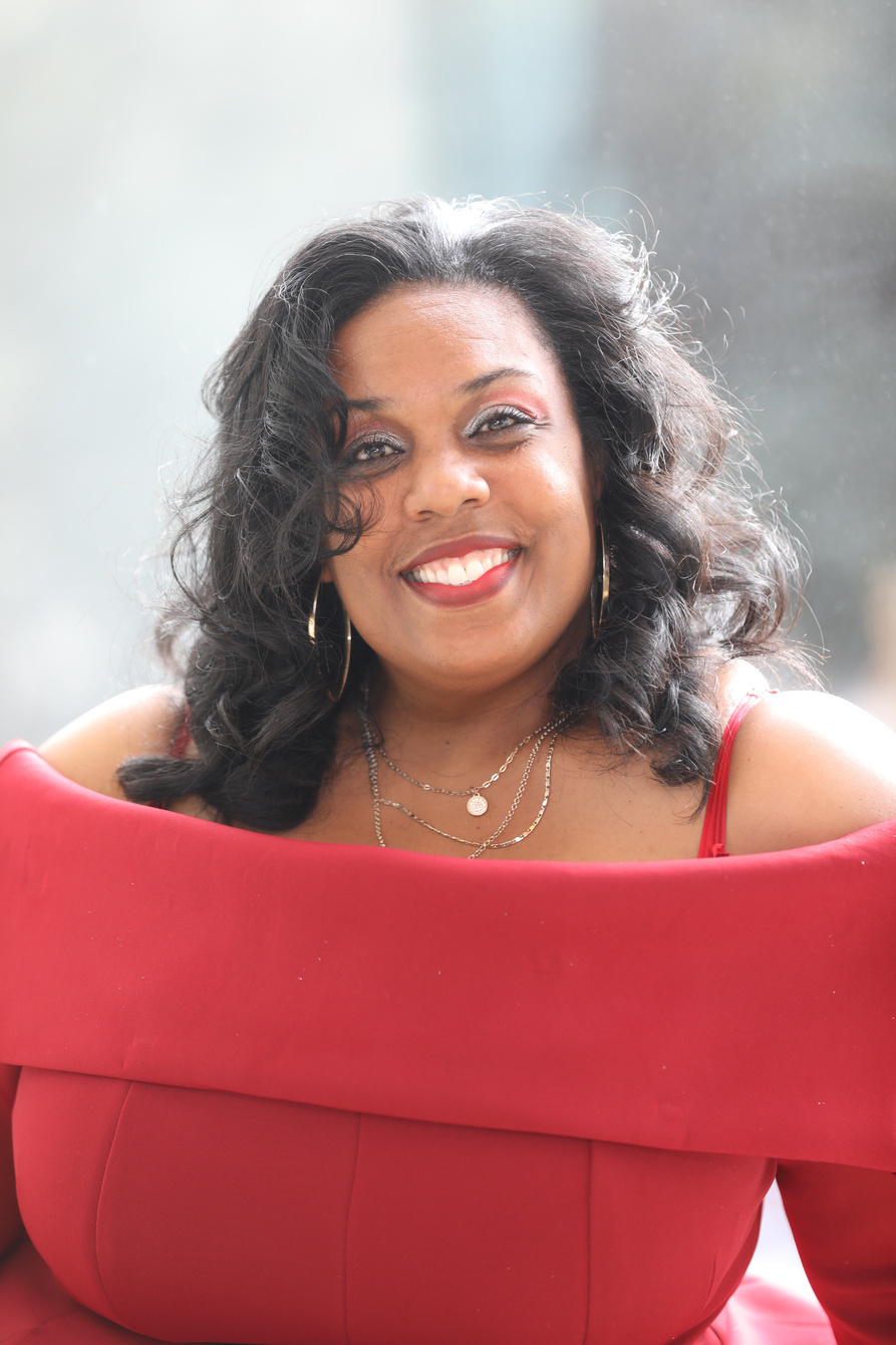 Profile headshot of the Author, Ieshea Hollins, who is a Black Woman with dark brown curly hair and is wearing a red top and a gold necklace.